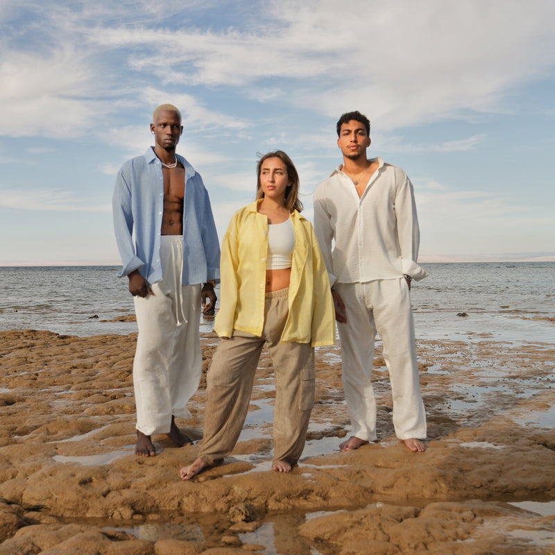 Three people standing on a rocky beach with ocean and sky in the background